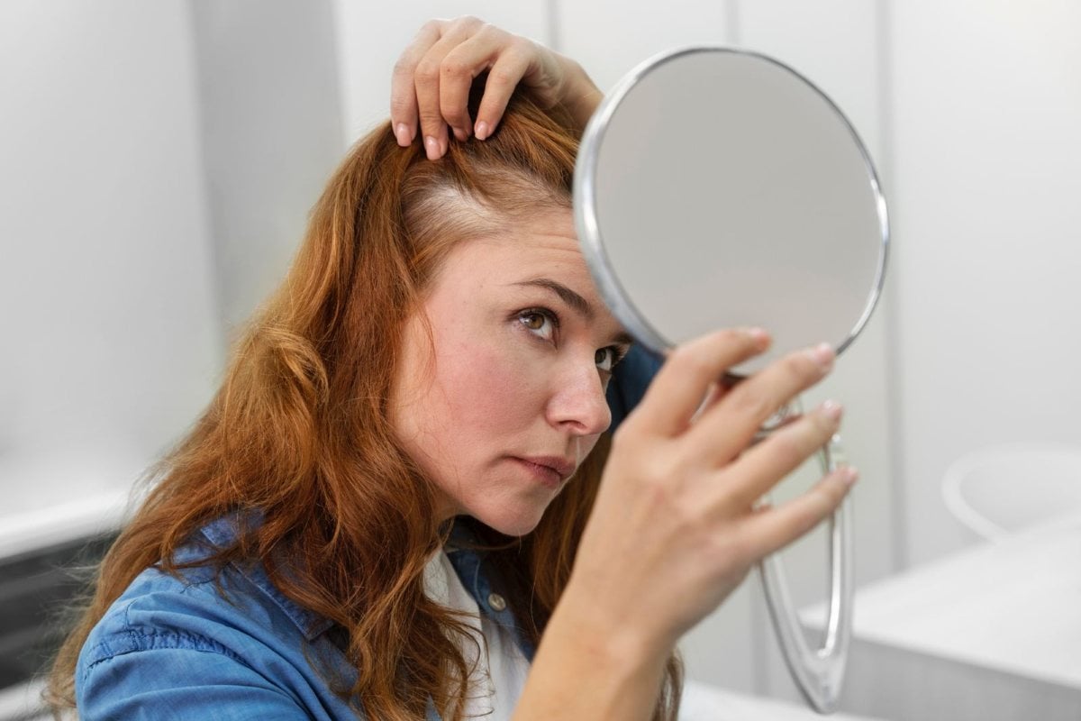 Mulher olhando o cabelo em espelho - queda de cabelo
