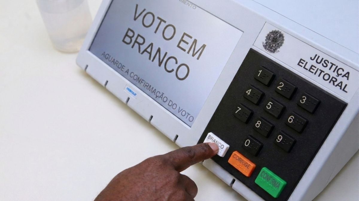 manual do eleitor pessoa apertando o botão branco da urna eleitoral eletrônica voto eleições 2026