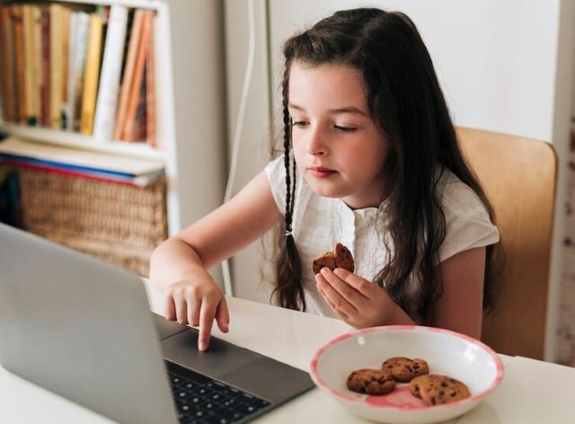 crianca-menina-garota-notebook-computador-lanche-biscoitos-foto-freepik