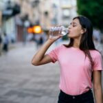 linda-garota-bebendo-com-uma-garrafa-de-agua-em-uma-rua-da-cidade_freepik