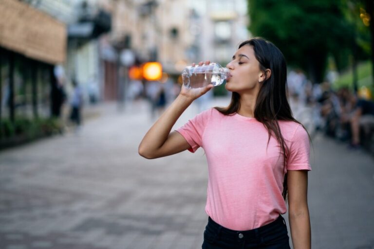 linda-garota-bebendo-com-uma-garrafa-de-agua-em-uma-rua-da-cidade_freepik