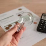 O5nahKFG-uma-mao-segurando-a-lampada-sobre-a-conta-de-eletricidade-varias-moedas-e-uma-calculadora-na-conta-conceito-de-precos-de-eletricidade-e-pagamento-de-impostos_704508-992