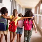 vista-traseira-de-estudantes-multirraciais-do-ensino-fundamental-com-mochilas-e-bracos-andando-no-corredor_13339-313034