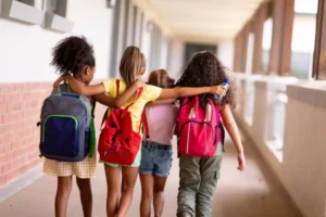 vista-traseira-de-estudantes-multirraciais-do-ensino-fundamental-com-mochilas-e-bracos-andando-no-corredor_13339-313034