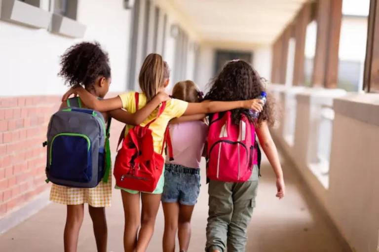vista-traseira-de-estudantes-multirraciais-do-ensino-fundamental-com-mochilas-e-bracos-andando-no-corredor_13339-313034