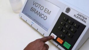 manual-do-eleitor-pessoa-apertando-o-botao-branco-da-urna-eleitoral-etetronica-voto-eleicoes-2026-foto-gerado-com-auxilio-de-IA