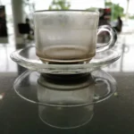 manchas-de-cafe-em-xicara-transparente-caneca-colocada-uma-mesa-marmore-preta-que-acaba-sem-vidro-clara-sai-o-reflexo-da-na-157212696