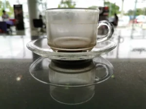 manchas-de-cafe-em-xicara-transparente-caneca-colocada-uma-mesa-marmore-preta-que-acaba-sem-vidro-clara-sai-o-reflexo-da-na-157212696